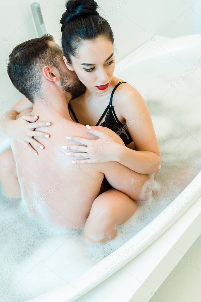 overhead view of bearded man kissing neck of attractive woman in bathtub 