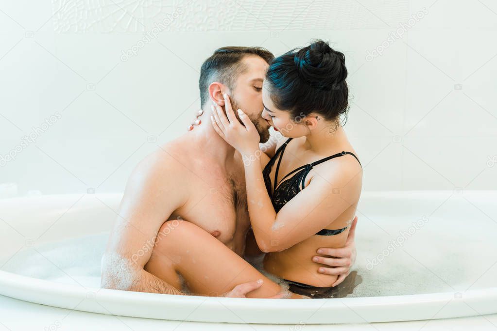 attractive and sexy woman kissing shirtless men in bathtub with foam 