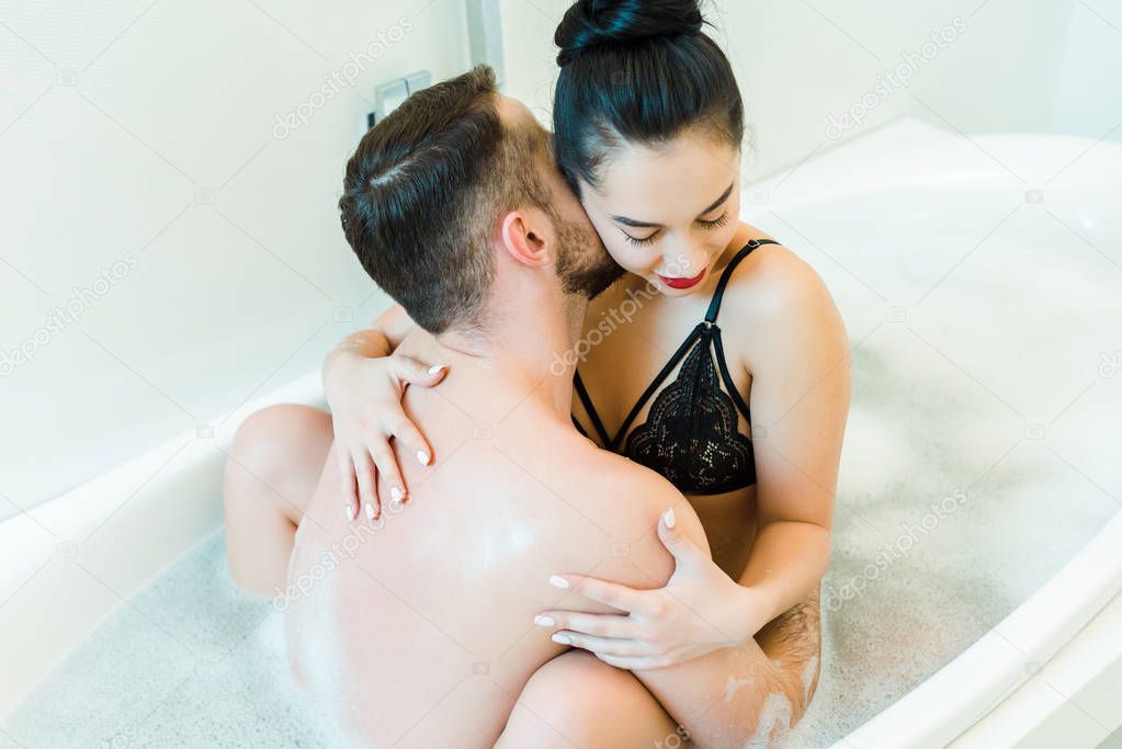 overhead view of bearded man kissing neck of young woman in bathtub 