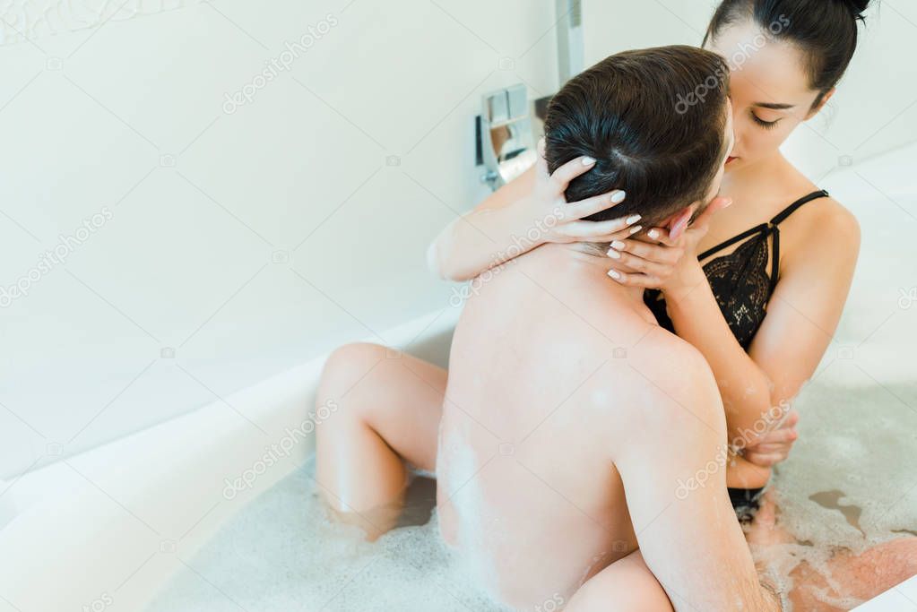 back view of bearded man kissing sexy young woman in bathtub 