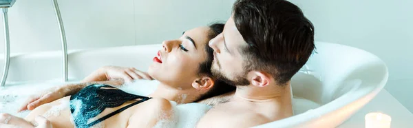 黑发年轻女子躺在浴缸中与胡子男子全景拍摄 — 图库照片