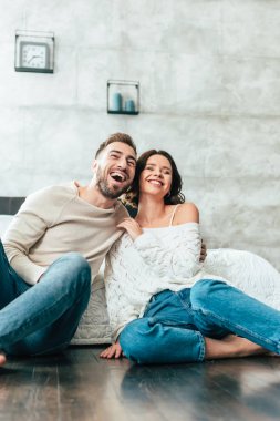 low angle view of happy man and woman sitting on floor and watching movie at home  clipart