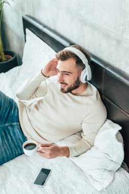 yatakta kahve bir fincan tutarken kulaklık müzik dinleneşeli adam havai görünümü 