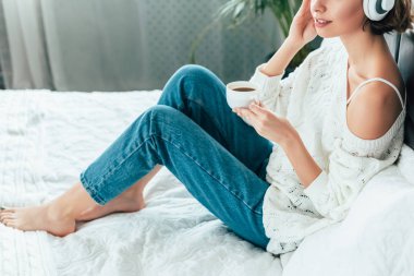 bardak tutan ve kulaklıkla müzik dinleyen kadının kırpılmış görünümü 