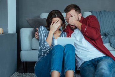 Kadın ve erkek dijital tablette video izlerken yüzlerini kapatıyorlar 