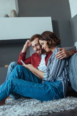halı üzerinde otururken akıllı telefon bakarak mutlu erkek ve kadın düşük açılı görünümü 
