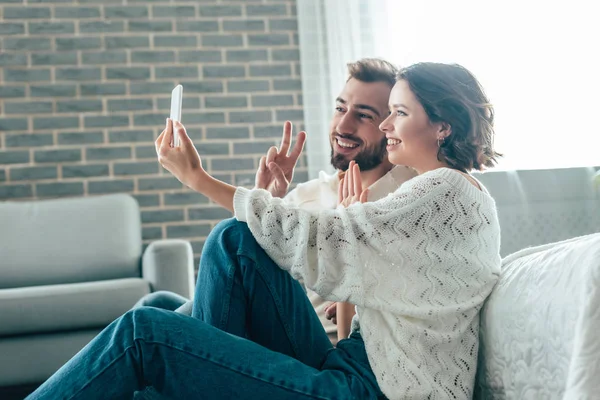 Happy Woman Waving Hand While Taking Selfie Man Showing Peace — Stock Photo, Image