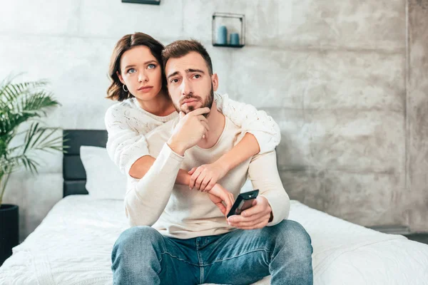 Attractive Woman Hugging Upset Man Sitting Bed Holding Remote Controller — Stock Photo, Image