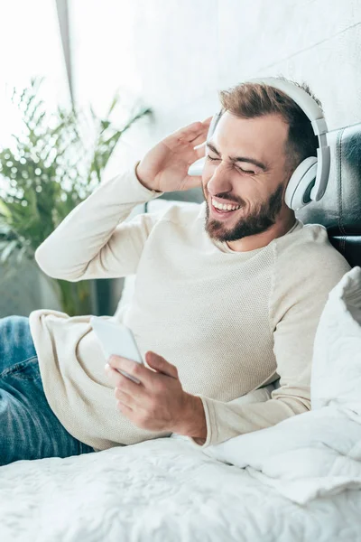 Happy Skäggiga Man Holding Smartphone Medan Lyssnar Musik Hörlurar — Stockfoto