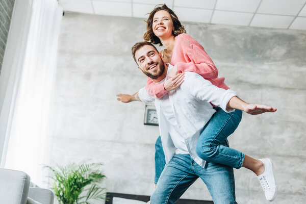 low angle view of happy bearded man piggybacking cheerful brunette woman 