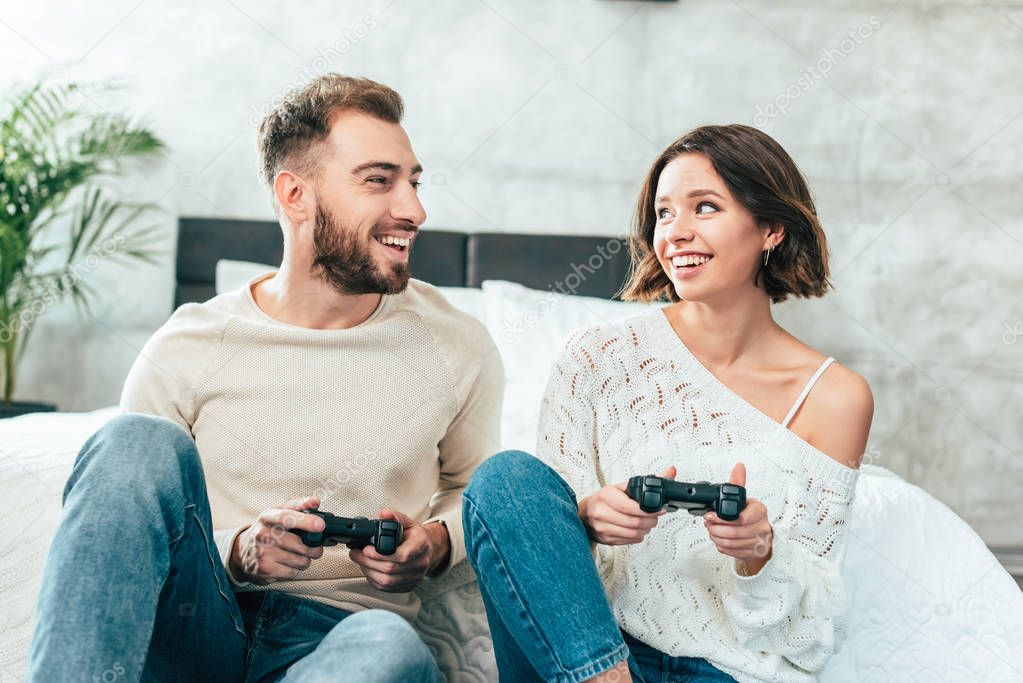 happy man looking at cheerful woman holding joystick at home 