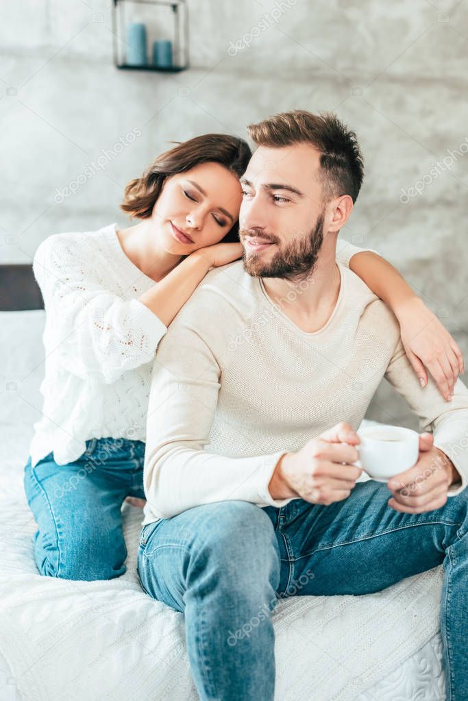 happy woman with closed eyes hugging happy man holding cup with coffee 