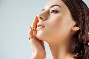 Parlak makyajlı ve altın yüzüklü genç bir kadın Gri renkte izole edilmiş yüzlere dokunuyor.