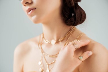 cropped view of young woman with shiny lips in golden necklaces and rings isolated on grey clipart
