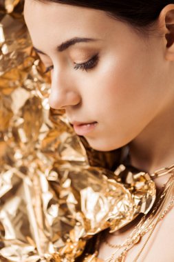young woman with shiny makeup and golden foil in necklaces posing with closed eyes clipart