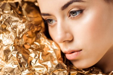 portrait of young woman with shiny makeup near golden foil looking away clipart