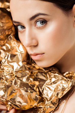 portrait of young woman with shiny makeup near golden foil looking at camera clipart