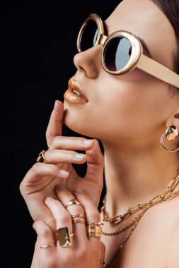 young nude woman in sunglasses, golden earring, rings and necklaces isolated on black clipart