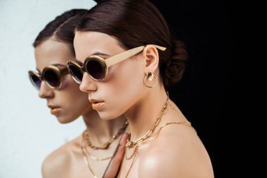 young naked woman in sunglasses, golden accessories holding mirror isolated on black clipart