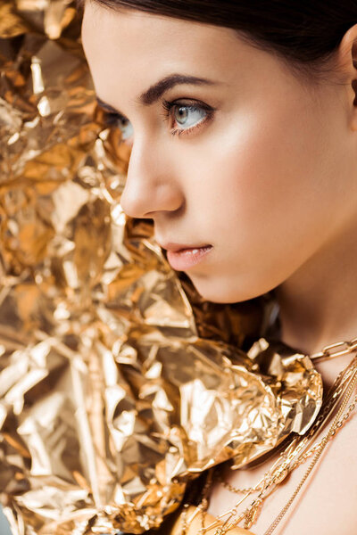 young woman with shiny makeup and golden foil in necklaces looking away