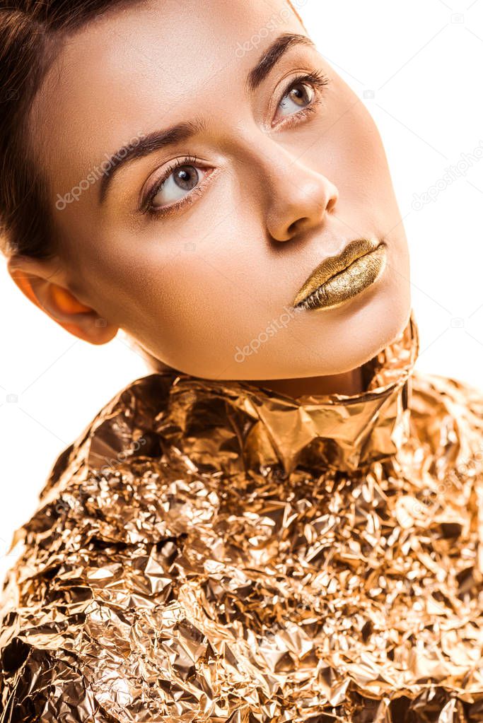 young beautiful woman with golden lips in golden foil looking away isolated on white