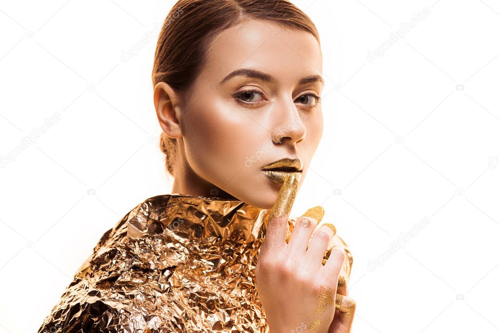 young beautiful woman in golden foil touching golden lips isolated on white