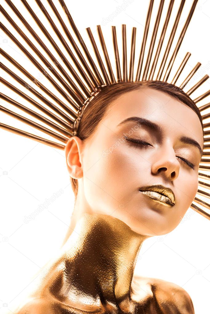 nude beautiful young woman painted in golden with accessory on head and closed eyes isolated on white
