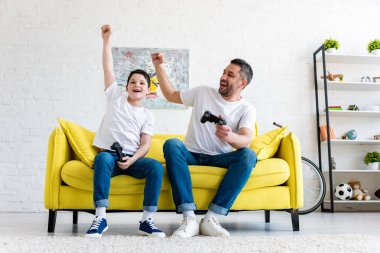 evde kanepede Video Oyunu oynarken baba ve oğlu tezahürat