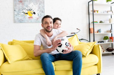 baba ve oğlu evde futbol topu ile kanepede spor maçı izlerken