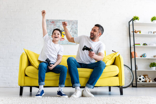 father and son cheering while playing Video Game on couch at home