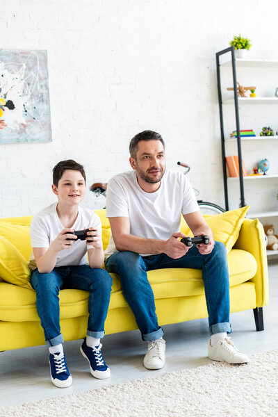 father and son with joysticks playing Video Game on couch in Living Room