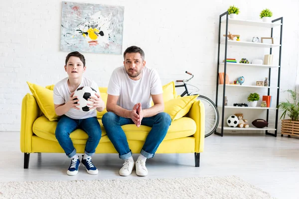 father and son watching sports match on couch at home with copy space