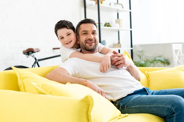 Son Looking Camera While Hugging Father Sitting Couch Home — Stock Photo, Image