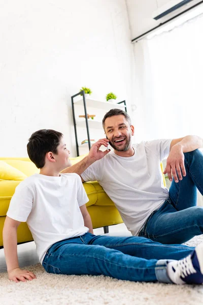 Filho Sentado Tapete Perto Pai Falando Smartphone Sala Estar — Fotografia de Stock