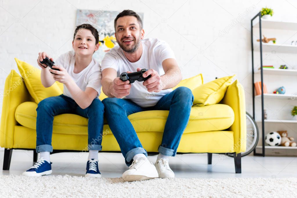 excited father and son playing Video Game on couch in Living Room