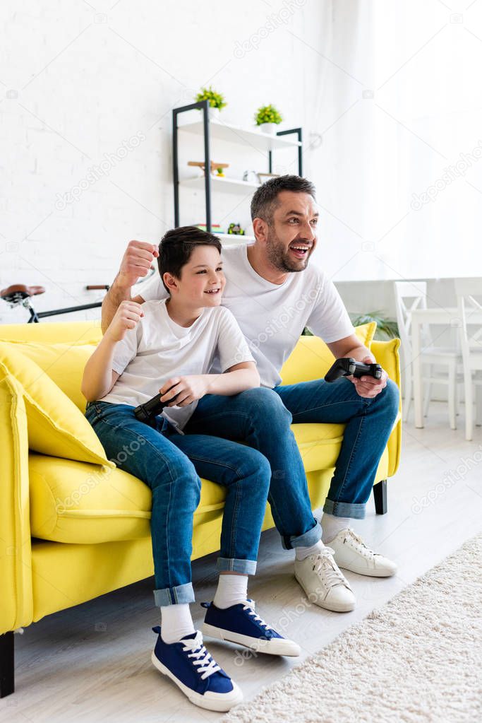 excited father and son cheering while playing Video Game on couch at home in Living Room
