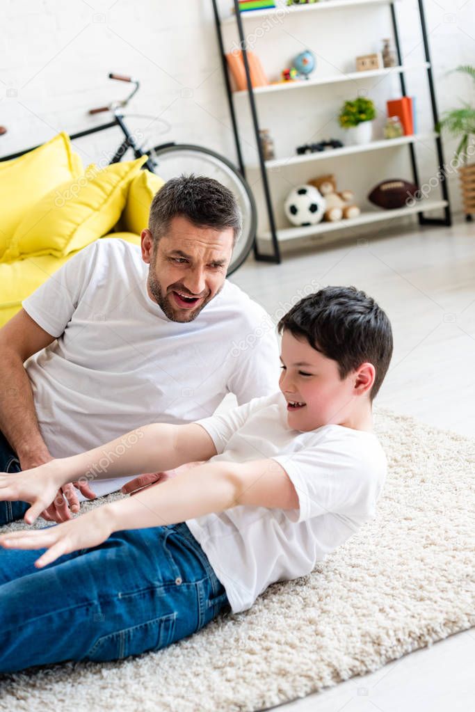 father looking at son doing sit up exercise on carpet at home