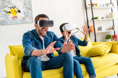vr kulaklıklar heyecanlı baba ve oğlu evde kanepede Sanal gerçeklik yaşıyor