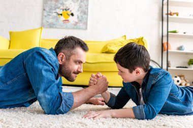 father and son lying on carpet and arm wrestling at home clipart