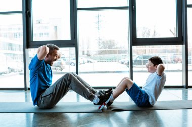 baba ve oğlu spor salonunda fitness paspaslar üzerinde egzersiz kadar oturup yapıyor