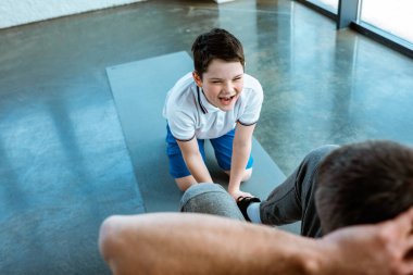 son shouting while helping father doing sit up exercise at gym clipart
