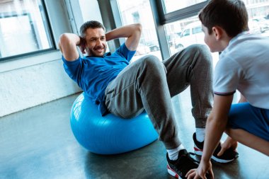 oğlu fitness topu üzerinde oturan ve spor salonunda egzersiz kadar oturmak yapıyor baba yardım