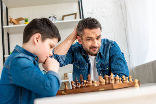 selective focus of father and son in denim playing chess at home