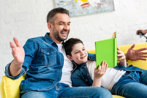 自宅のソファでデニム読書本で笑顔の父と息子 — ストック写真