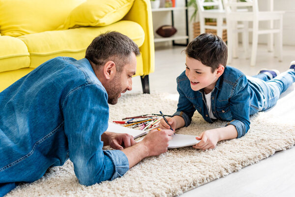 father and son lying on carpet and drawing in Living Room