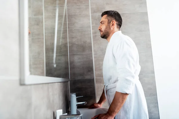 Hombre Guapo Albornoz Blanco Mirando Espejo Baño Durante Rutina Mañana — Foto de Stock