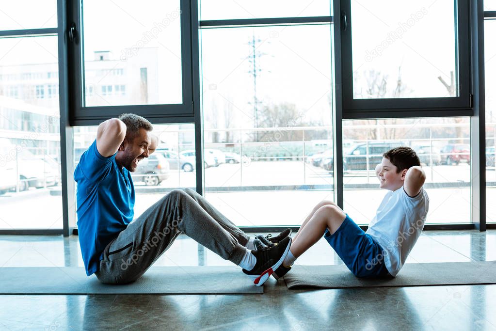 father and son doing sit up exercise on fitness mats at gym