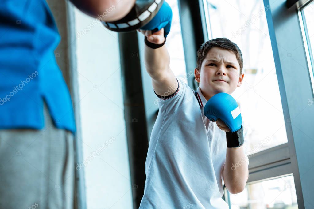 selective focus of boy in boxing gloves training with coach at gym