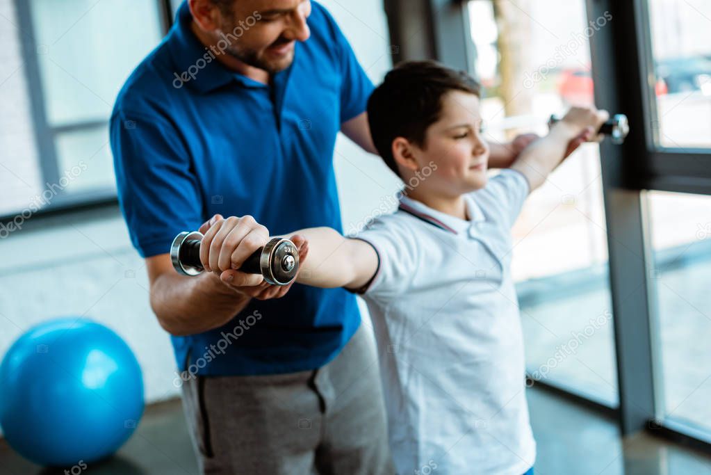 father helping son working out with dumbbells at gym