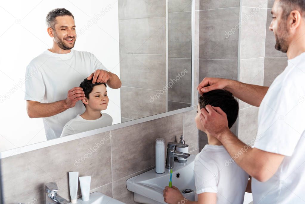 happy father adjusting hairstyle of son in bathroom in morning